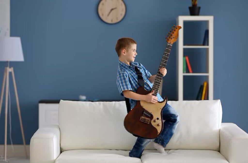 Menino em pé sobre um sofá, tocando uma guitarra infantil de modelo profissional: uma entre várias opções disponíveis no mercado.